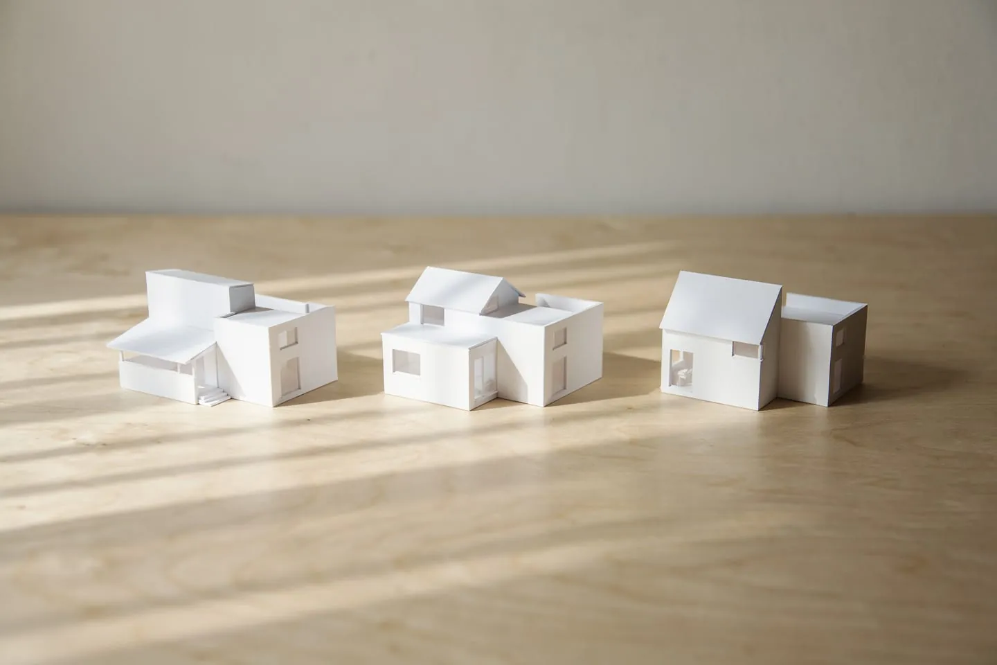 Drei weiße Kartonmodelle desselben Hauses, die unterschiedliche Anordnungen seiner Baukörper zeigen